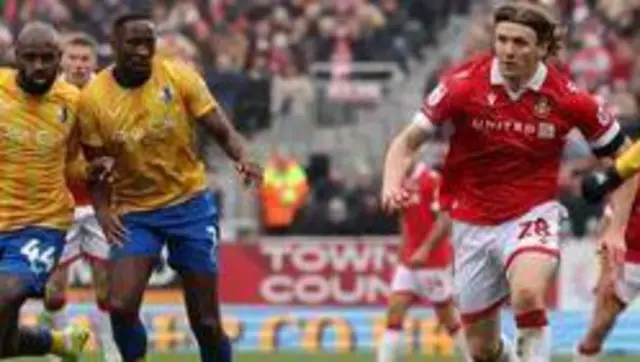 Jon Dadi Bodvarsson runs with the ball for Wrexham as he is tracked by yellow-shirted Mansfield players