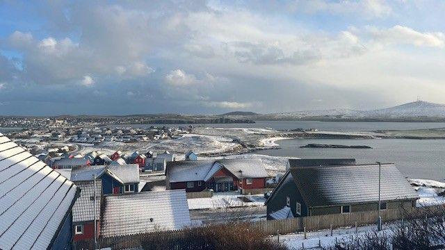 An image of snow-covered roofs in Shetland, with snow on hilltops in the distance, beyond a body of water.