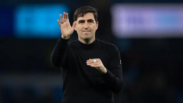 Andoni Iraola waves to Bournemouth's fans. He wears all black.