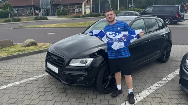 Chelsea fans stands with flag in front of car