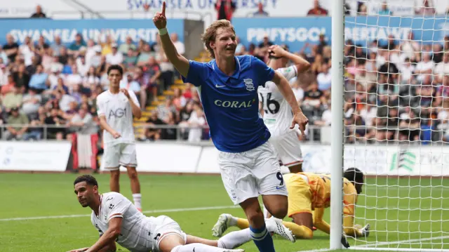 August Priske, wearing Birmingham City's blue home shirt, celebrates scoring against Swansea City in the EFL Cup by holding his hand up in the air and pointing