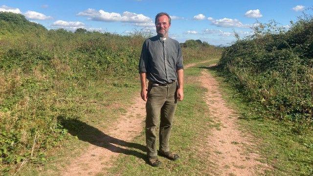 Paul Cawthorne standing on a former landfill site - a dirt track leads around the corner, with bushes either side