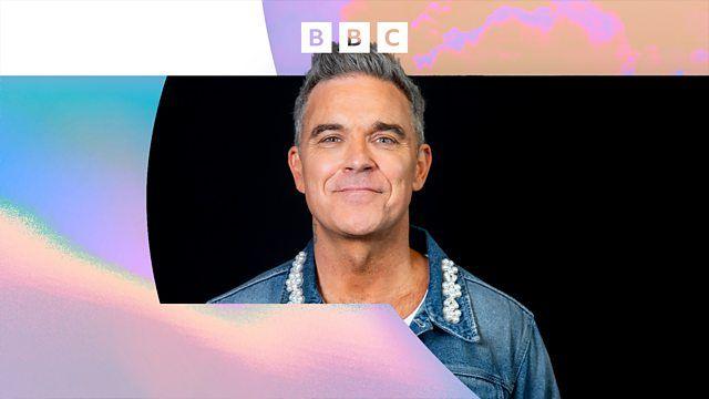 A BBC-branded image with Robbie Williams pictured, smiling at the camera and wearing a denim jacket, pictured against a black background with multi-coloured branding protruding from the sides.
