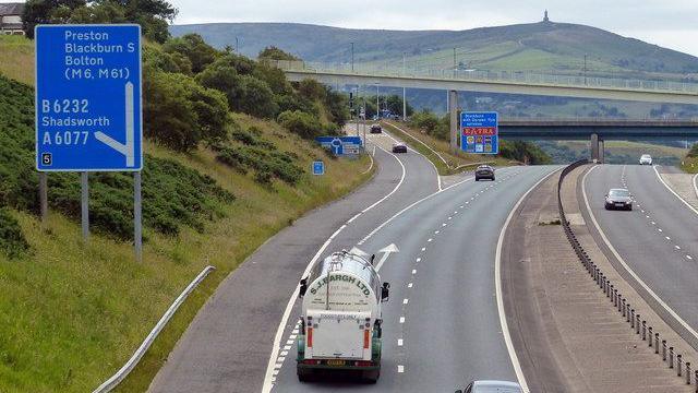 Vehicles on either side of the M65 at a slip road junction, with Darwen Hill and the Jubilee Tower on the summit in the background