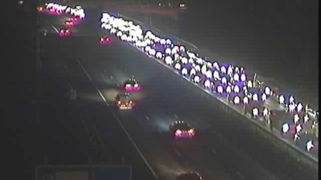 Cars on a carriageway. Their headlights are bright as it is dark and they are lined up three-deep in traffic. The opposite carriageway is clear with cars moving freely.