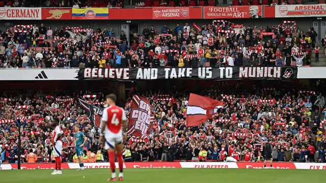 Arsenal fans hold a large sign that reads: 'Believe and take us to Munich'