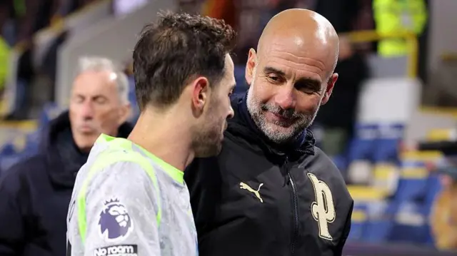 Pep Guardiola, Manager of Manchester City, speaks with Bernardo Silva
