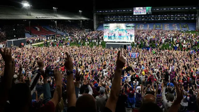Fans invade the pitch at Selhurst Park where a big screen shows Palace enjoying success in Germany
