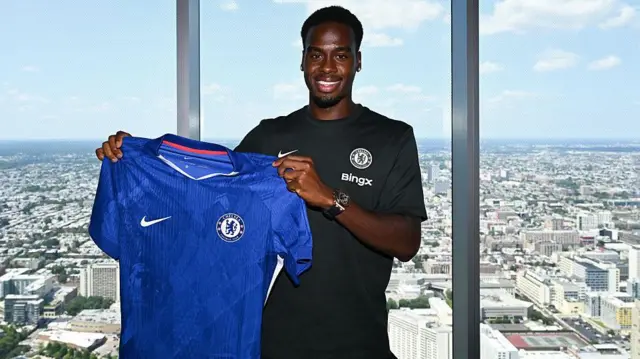 Jamie Gittens holds the Chelsea shirt up