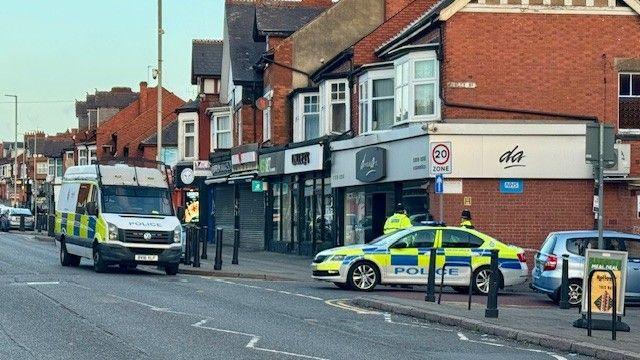 A police van and a police car on a street with shops on.