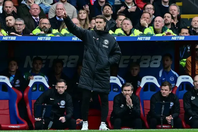 Fabian Hurzeler standing on the touchline issuing instructions to his players during Brighton's game against Crystal Palace. His backroom staff and substitutes are on the bench behind him, as are the first couple of rows of the crowd