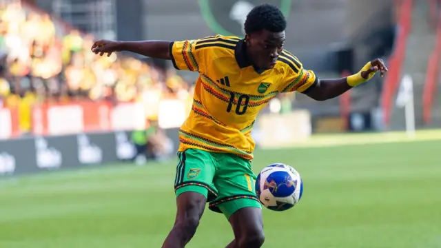 Kaheim Dixon in a yellow Jamaica shirt and green shorts controls the ball during the game against India