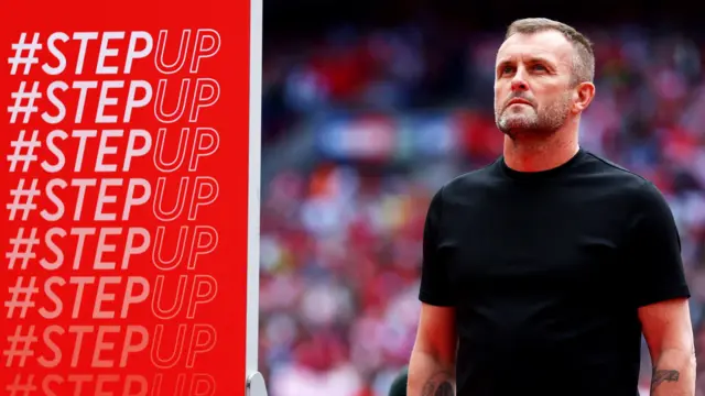 Charlton Athletic manager Nathan Jones stands next to a Step Up banner on the pitch following promotion at Wembley in May