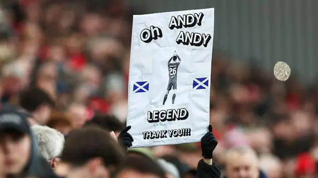 A fan of Liverpool displays a sign in support of Andrew Robertson reading "Oh Andy Andy Legend thank you" 