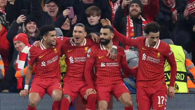 Liverpool players sit on advertising board and celebrate goal