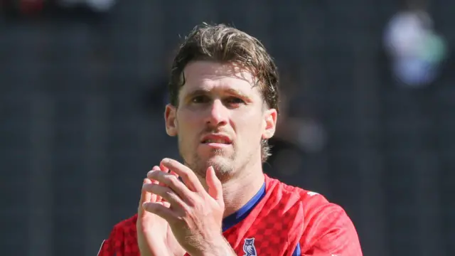 Reagan Ogle clapping Oldham fans at the end of a match wearing a red away kit