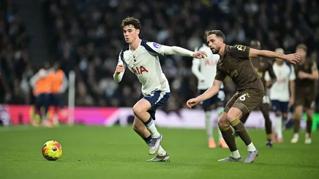 Archie Gray of Tottenham Hotspur dribbles away from Jordan Henderson of Brentford
