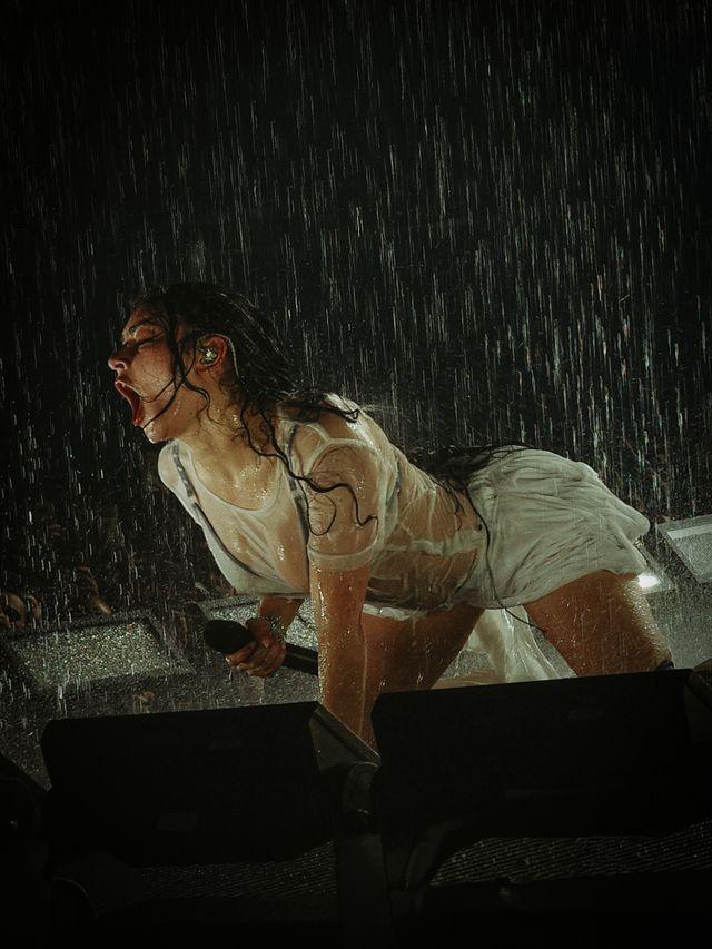 Charli XCX in a white, short outfit on all fours being showered with water on stage