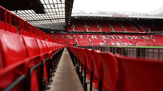 Old Trafford's empty Stretford End with blurred red seats in another stand in the foreground