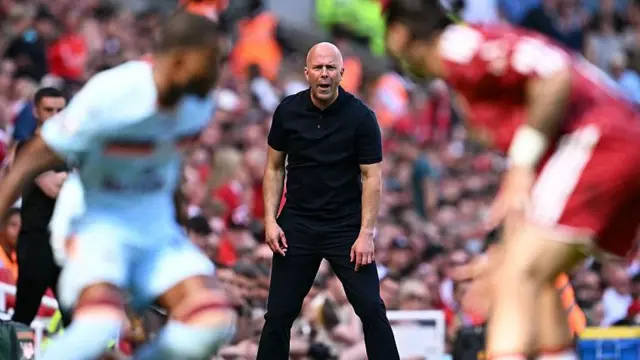 Arne Slot on the touchline at Anfield with two out of focus players in the foreground