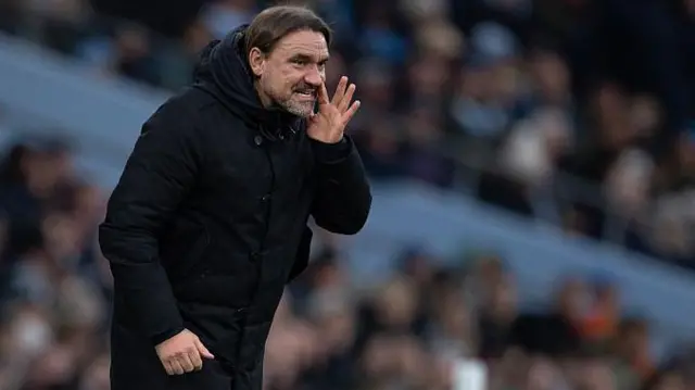Daniel Farke, wearing a black coat on the touchline and shouting instructions to his players
