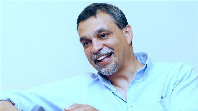  Aneez Esmail smiles while talking wearing a white shirt.