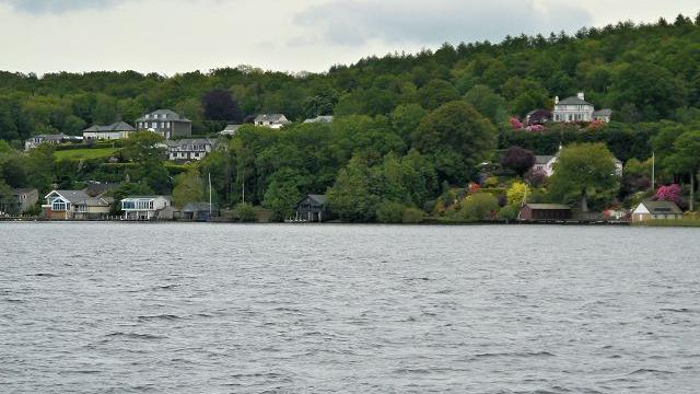 Eastern shore of Windermere in the Lake District. It has a few houses and boat houses dotted in between a forest. 