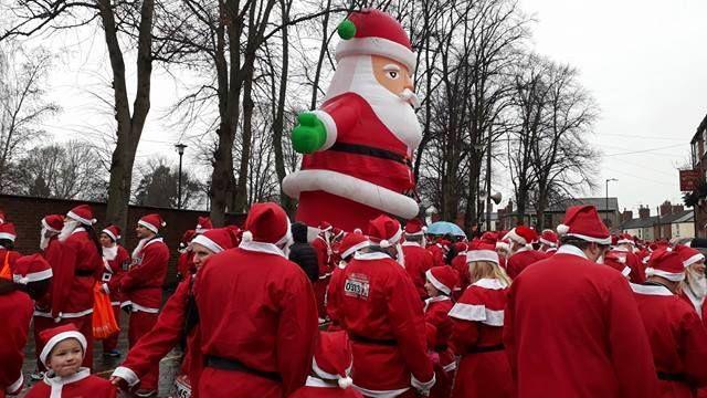 Dozens of people dressed in red and white Father Christmas outfits waiting to run. Some of them are wearing fake white beards.