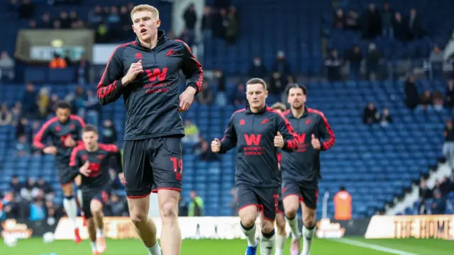 A photo of Millwall players running to warm up in their black and red away kits