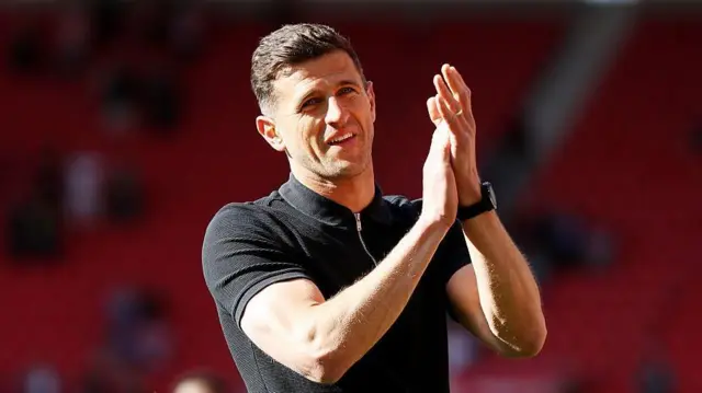 Portsmouth boss John Mousinho wearing a black short sleeved top applauding supporters after a win at Middlesbrough