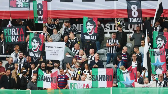 Fans of Newcastle United hold up signs and banners showing their support for Sandro Tonali