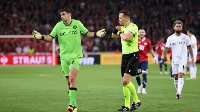 Emiliano Martinez of Aston Villa reacts after being shown a yellow card by Referee Ivan Kruzliak during the UEFA Europa Conference League 2023/24 Quarter-final second leg match between Lille OSC and Aston Villa