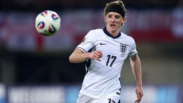 Anthony Gordon, in England's white home kit and a headband, chases a loose ball during a match