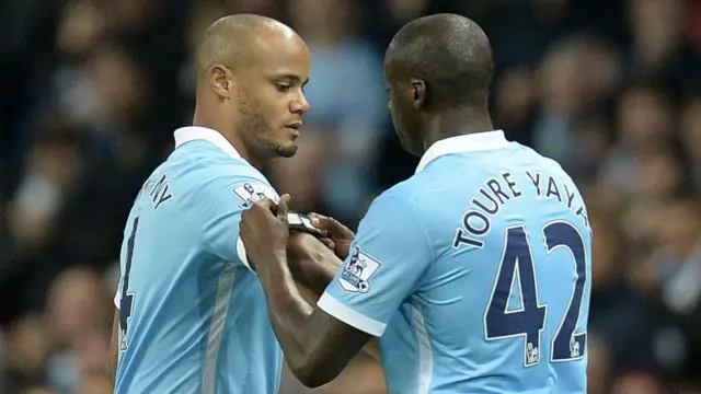 Yaya Toure places an armband on Vincent Kompany. Toure wears a number 42 shirt