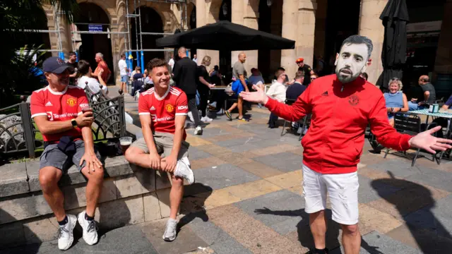 A group of Manchester United fans, with one wearing a Bruno Fernandes mask