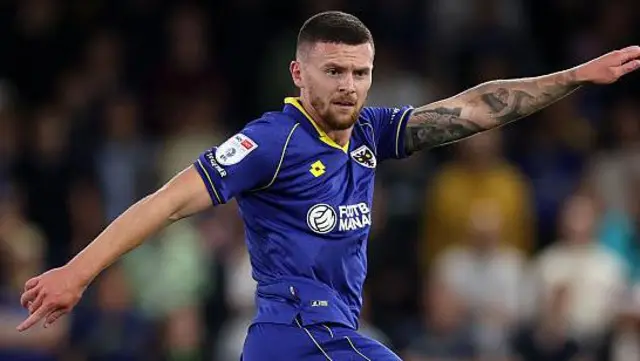 Josh Kelly in all blue Wimbledon kit with both arms out in opposite directions