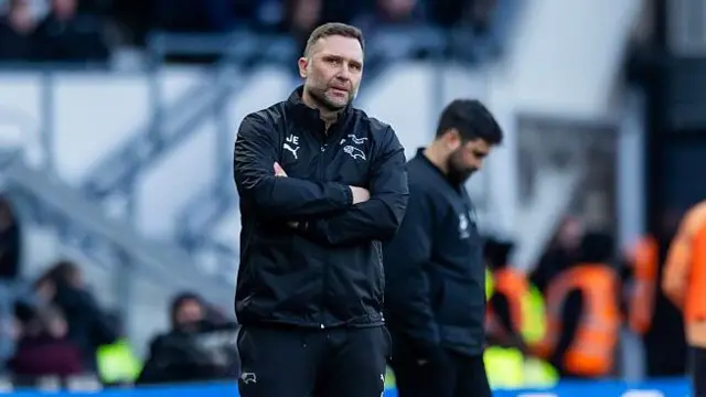 John Eustace, arms folded, on the touchline with Vitor Matos, head bowed, in the background 