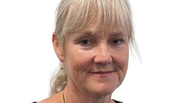 Person with blond hair and wearing earrings looks at camera