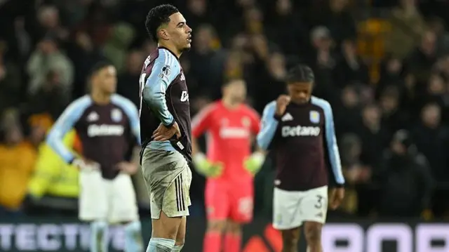 Morgan Rogers looks dejected on the pitch, with three other Aston Villa players out of focus in the background