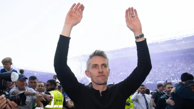 Kieran McKenna, with both arms aloft, looking up into the stands after Ipswich had secured promotion as security hold back fans behind him