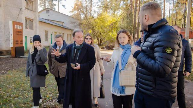 The council leader has short dark hair and is wearing a green scarf and navy coat. He is walking with a group and talking to a tall man with short hair and a black coat on