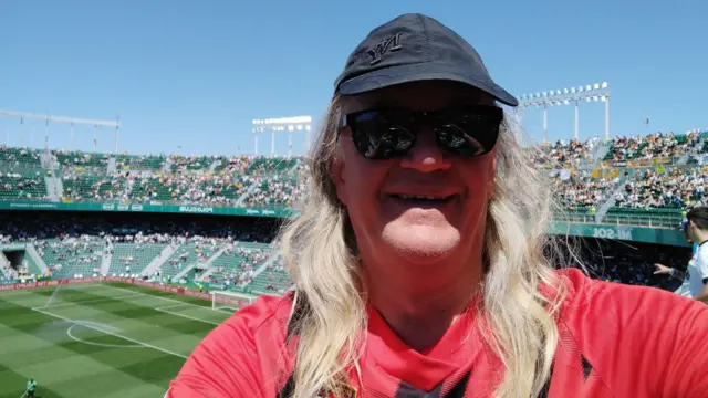 A picture of a 72-year-old man at a football stadium wearing a red and black Bournemouth shirt