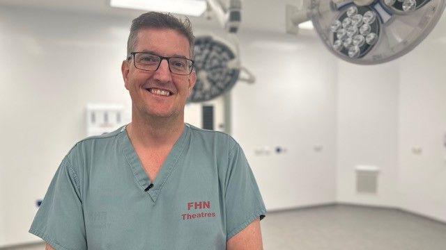 Consultant Craig White, dressed in blue scrubs, stands in a new operating theatre.