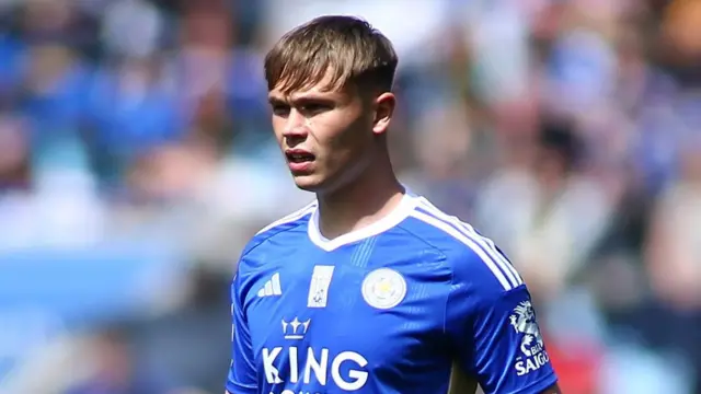 Callum Doyle, wearing Leicester's blue home kit, looks towards the left of the image with the picture cutting off at the chest. He is squinting because the sun is shining in his face.