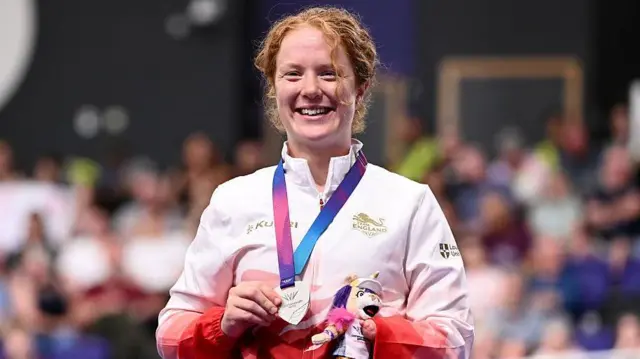 Morgan Newberry stands on the podium with her silver medal in her hand and holding a small mascot toy.