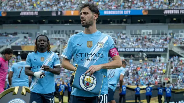Bernardo Silva holds a Manchester City pennant on the pitch before Thursday's game against Juventus