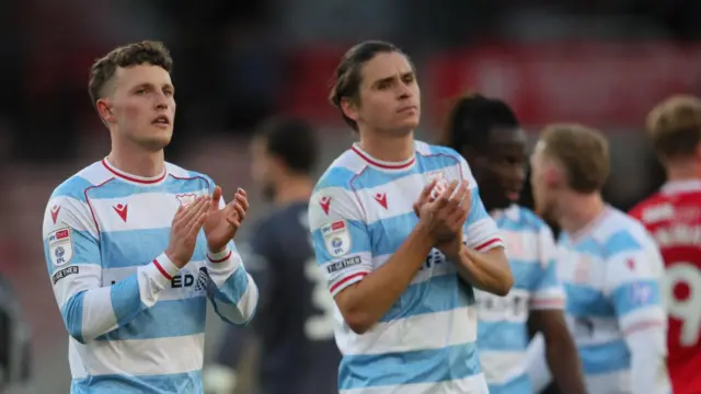 Nathan Broadhead and George Dobson in Wrexham's light blue and white away kit appluading fans