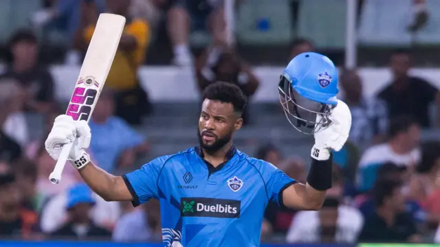 Shai Hope raises his bat and helmet after hitting a century for Pretoria Capitals
