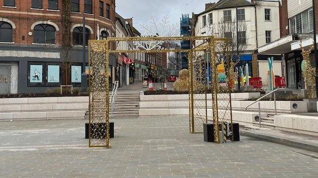 A gold decorative Christmas trellis stands in the middle of a newly renovated square in Yeovil town centre. Concrete seating is around the perimeter with staircases running up the middle of each side.