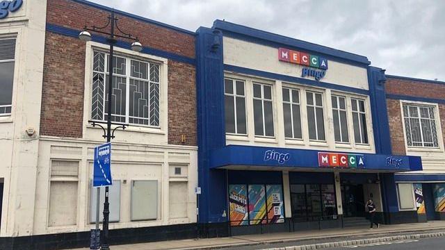 A 1930s Art Deco-style brick building with white and blue moulding. On the front are signs for Mecca Bingo.
